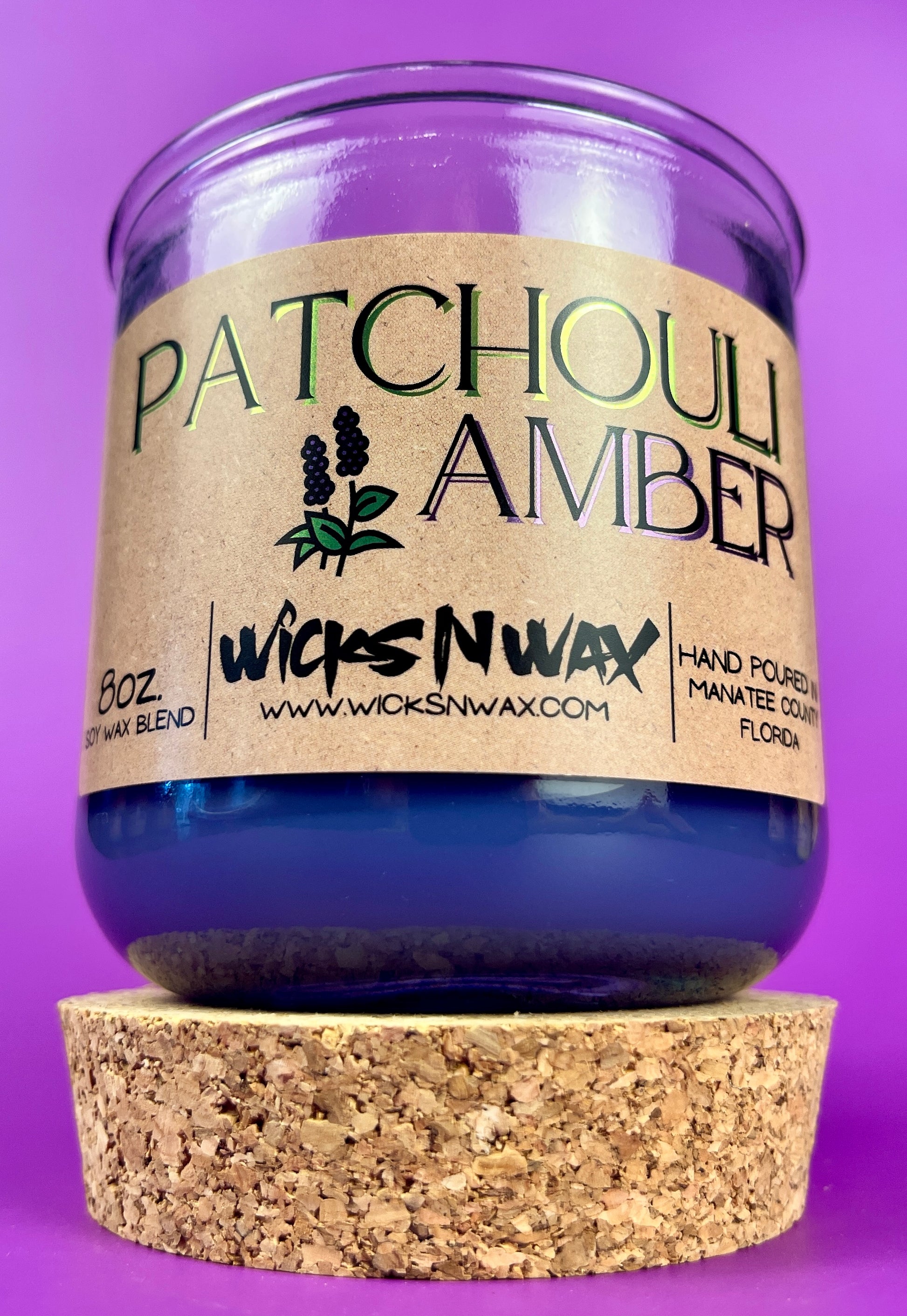 Recycled glass candle in clear jar with purple wax, cork coaster beneath.