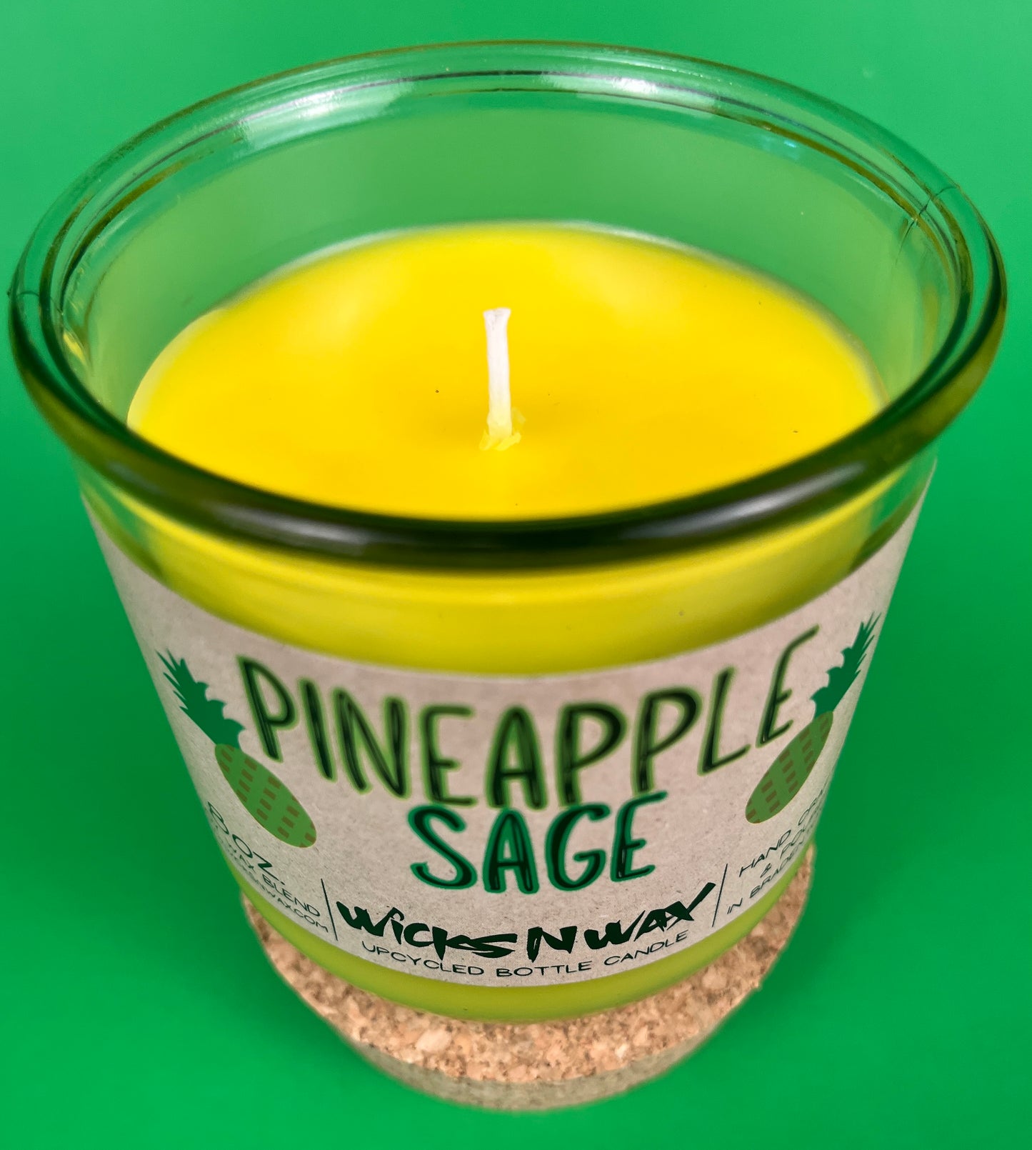 Pineapple Sage recycled glass candle with lit wick and yellow wax inside clear green jar