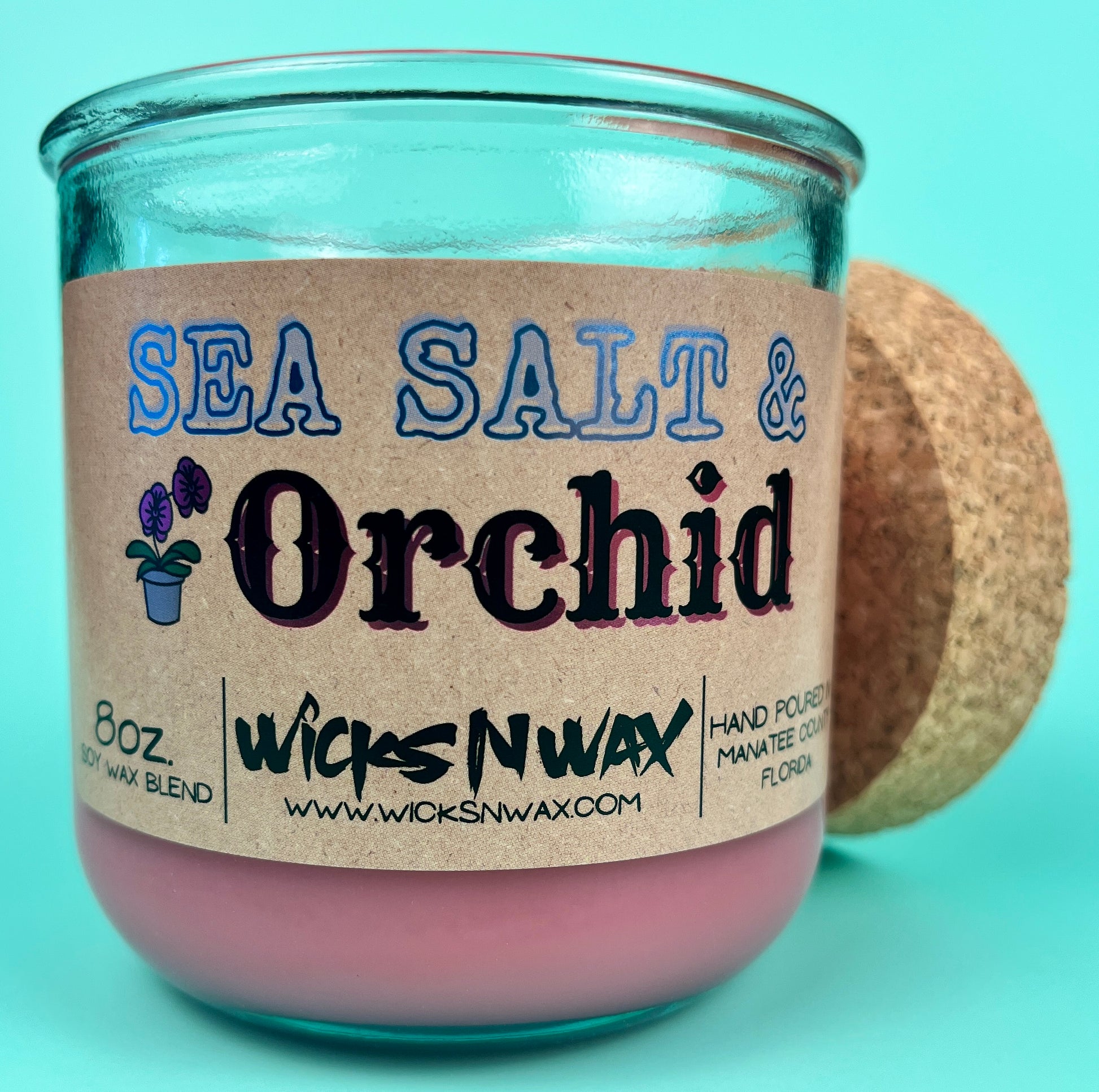 Recycled glass candle front view, pink wax, blue-and-black printed label, cork behind