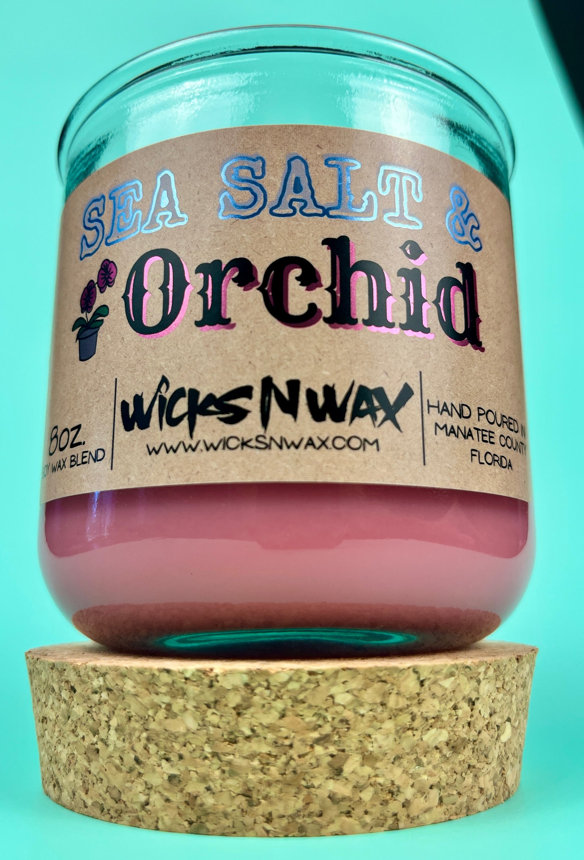 Recycled glass candle with cork lid below, pink wax, blue-and-black printed label