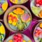 Multiple metal tins of sea-themed wax candles with orange, pink, yellow, and green shapes