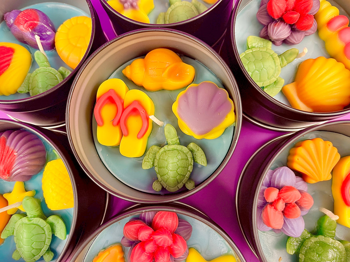 Multiple metal tins of sea-themed wax candles with orange, pink, yellow, and green shapes