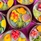 Assorted sea-themed wax candle tins with purple, orange, green, and red flower pieces