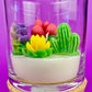 WicksNWax cactus art candle in clear glass with green, purple, yellow, and pink wax cacti
