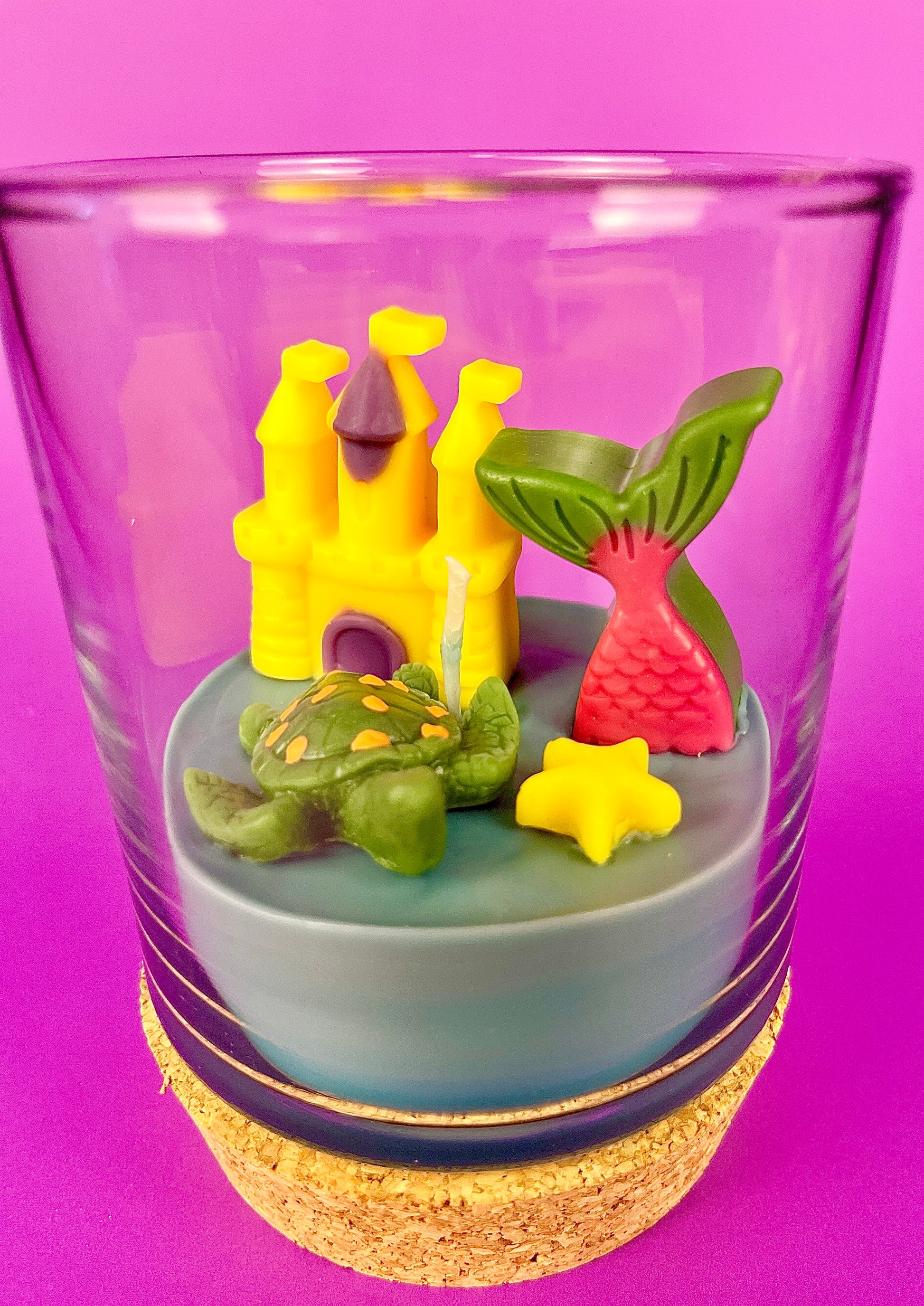 Small candle in glass with cork base, featuring castle and sea-creature wax