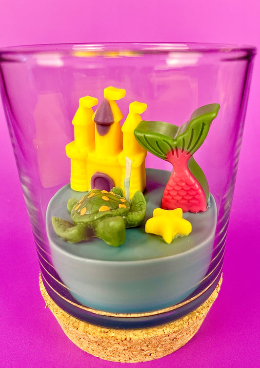 Small candle in glass with cork base, featuring castle and sea-creature wax