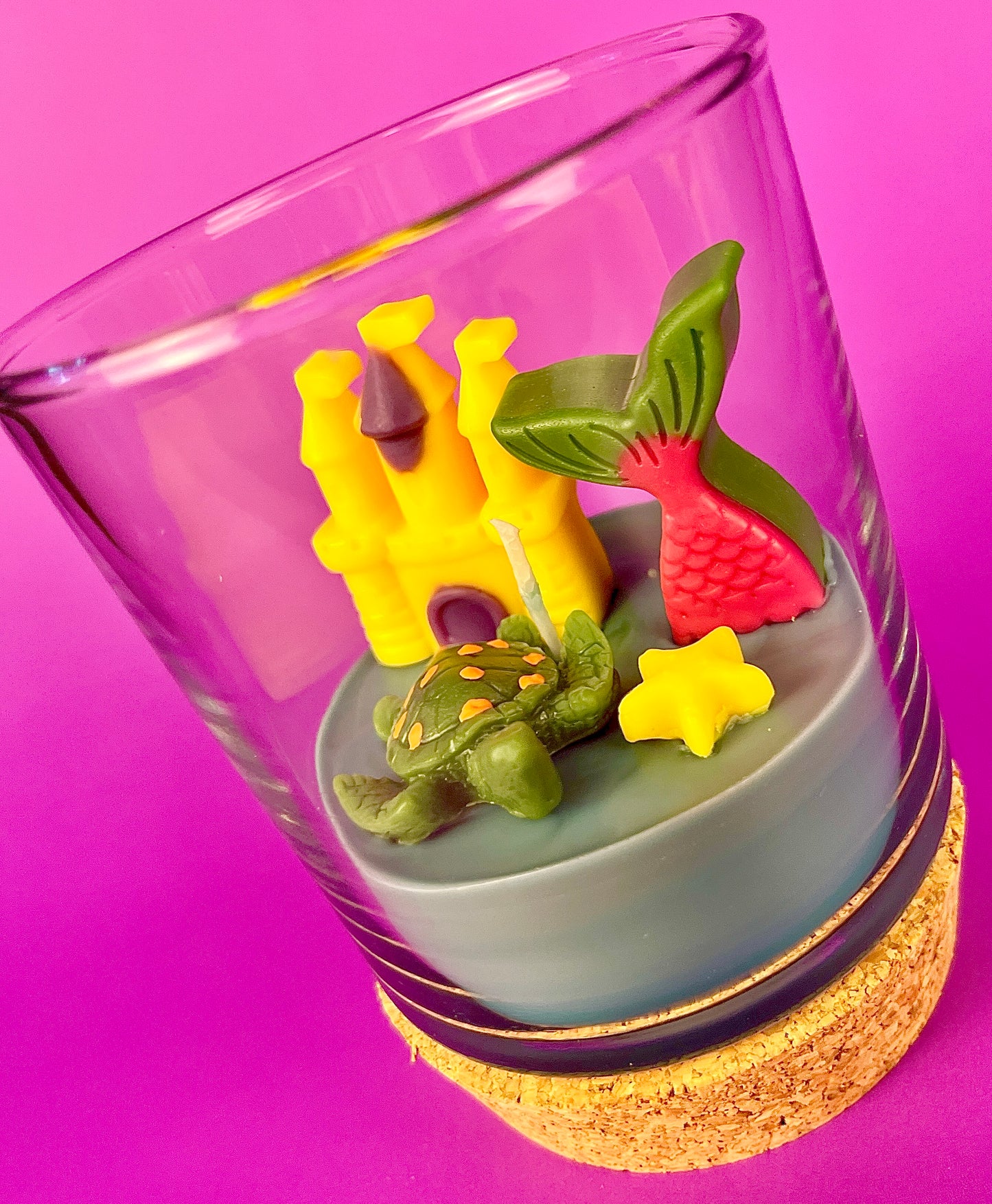 Small candle in glass with cork base, showing castle and star-shaped wax pieces