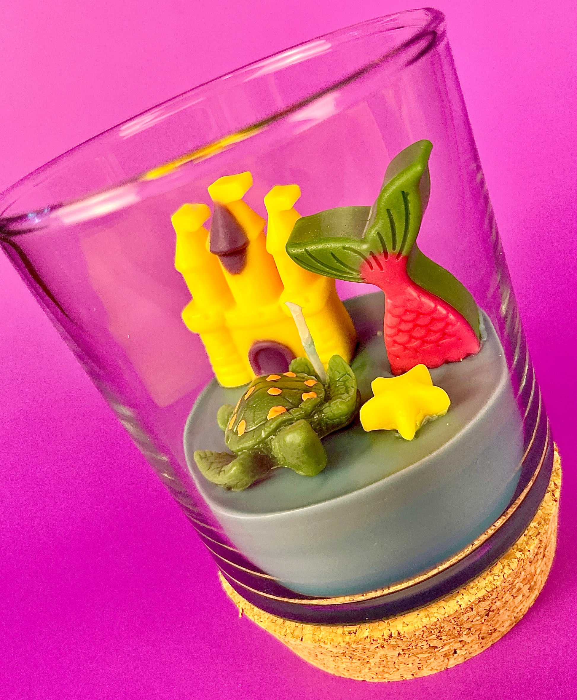 Small candle in glass with cork base, showing castle and star-shaped wax pieces