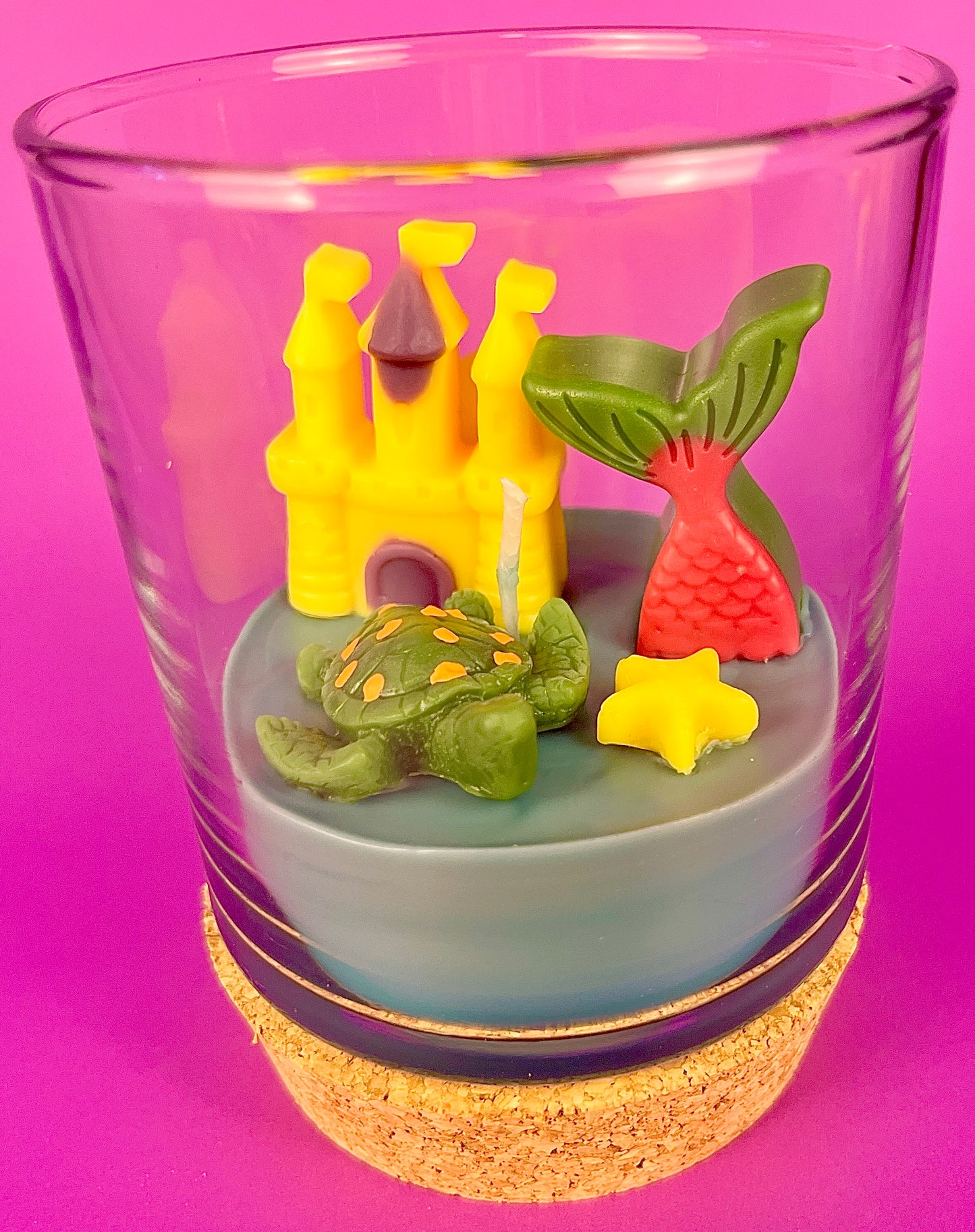 Small candle in glass with cork base, featuring castle and mermaid-shaped wax
