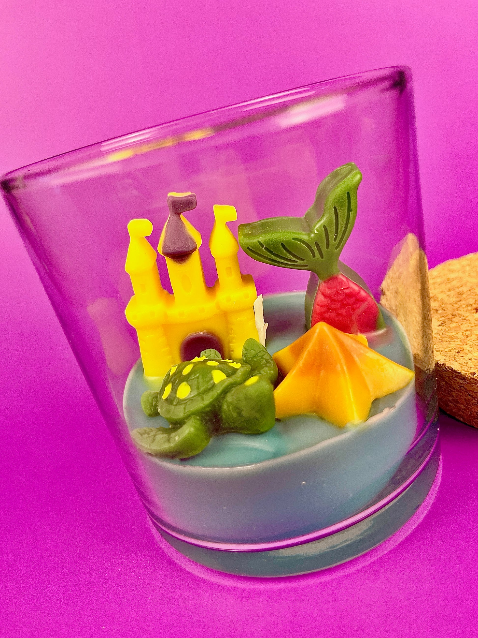 Small candle in glass container with pineapple, fish, and star-shaped wax pieces