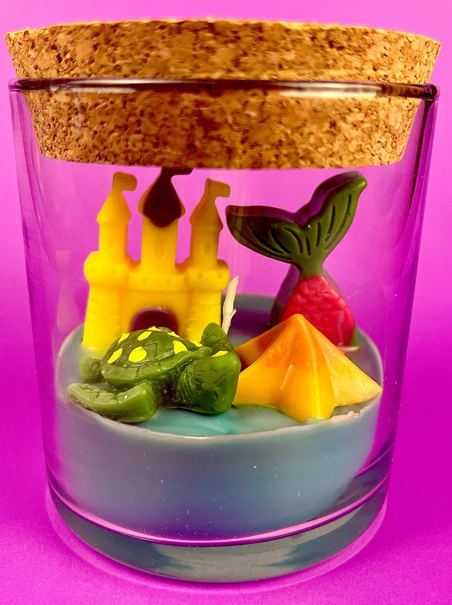 Small candle in glass container with castle, pineapple, and star-shaped wax pieces