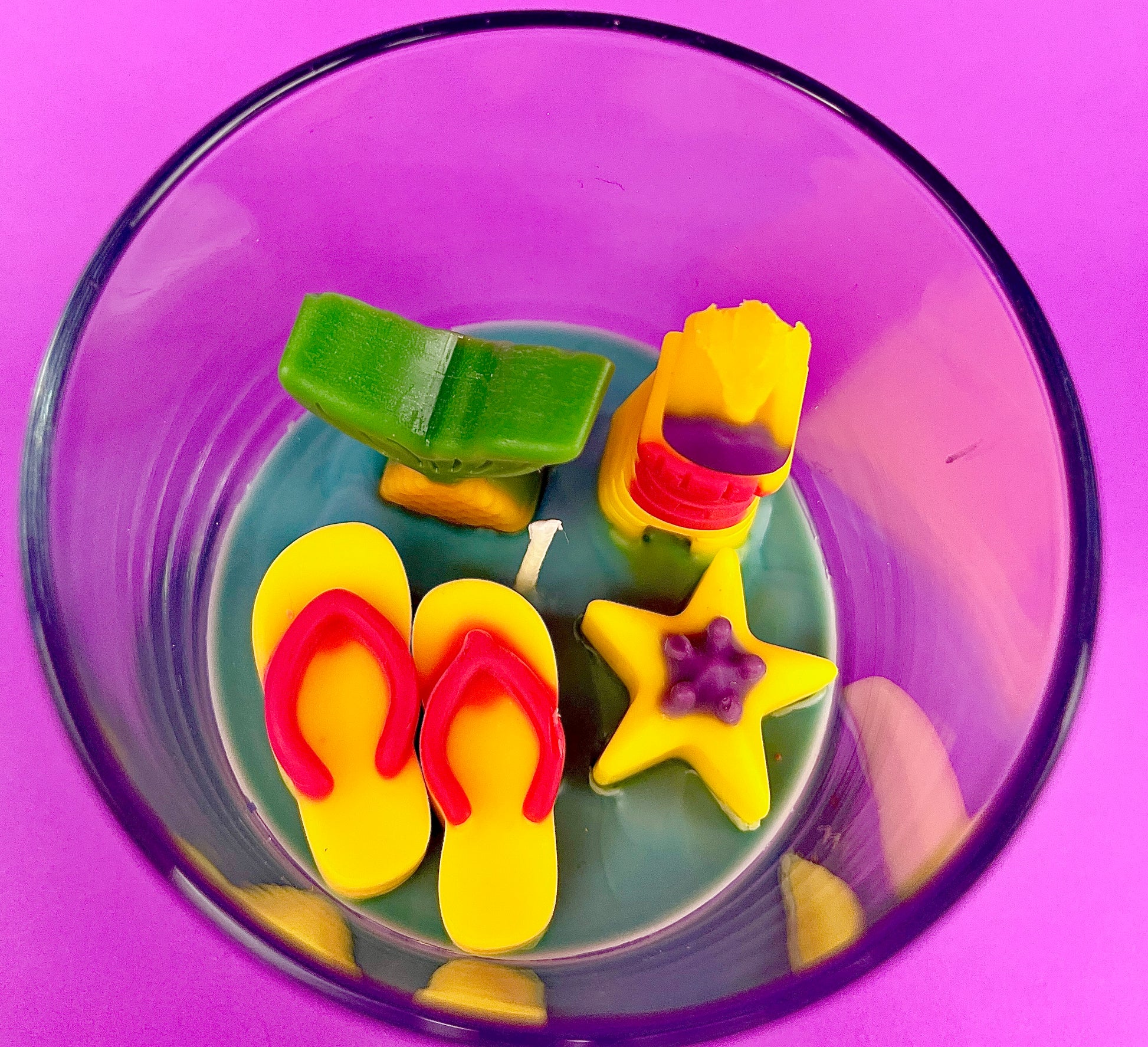 Small candle in glass container with colorful seashell-shaped wax pieces inside