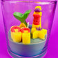 Small scented candle in clear glass jar with red-yellow lighthouse and yellow shell wax pieces