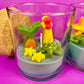 Small scented candle in clear glass jar with green leaf and red-yellow lighthouse wax topper
