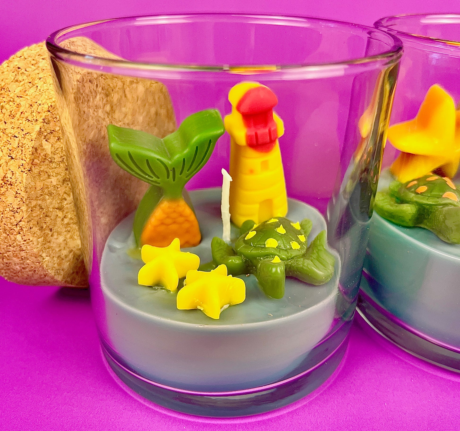 Small scented candle in clear glass jar with green leaf and red-yellow lighthouse wax topper