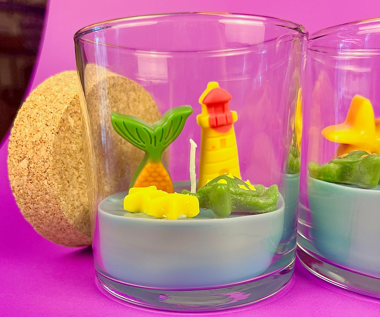 Small scented candle in clear glass jar with lighthouse, green leaf, and star wax pieces