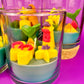 Small candle in glass container with stacked shapes: stars, shells, and castle