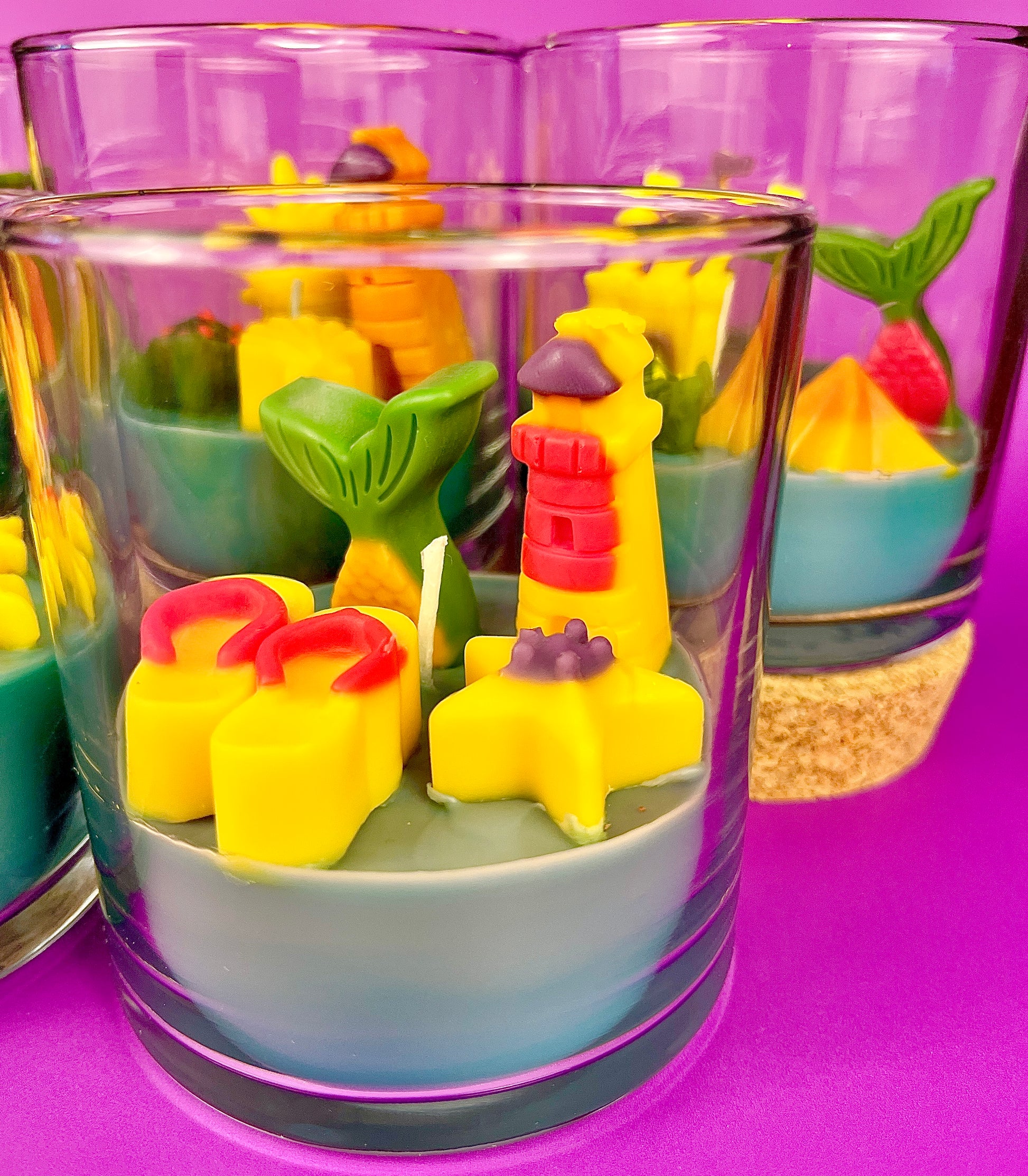 Small candle in glass container with stacked shapes: stars, shells, and castle