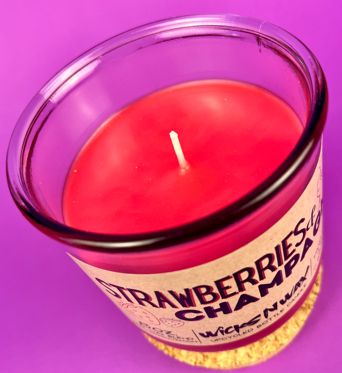 Red wax candle in clear glass jar, small white wick visible.