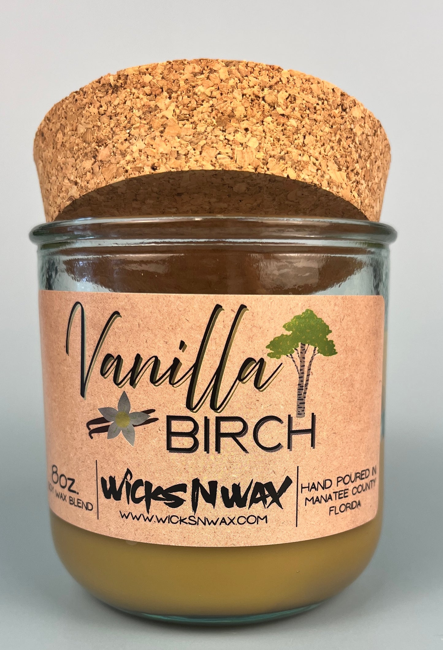 Vanilla Birch recycled glass candle with tan wax, clear glass jar, and cork lid behind label