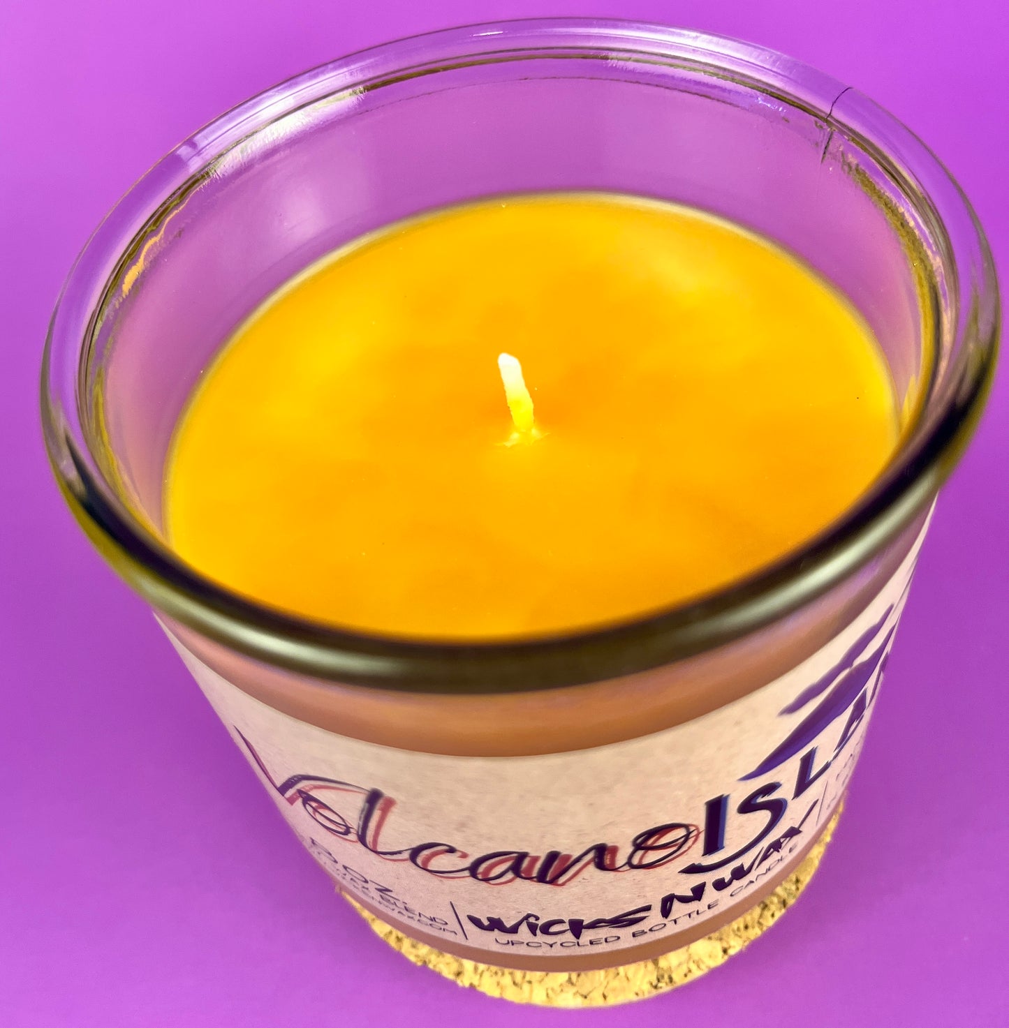 Yellow wax candle close-up with small flame wick inside Volcano Island glass jar