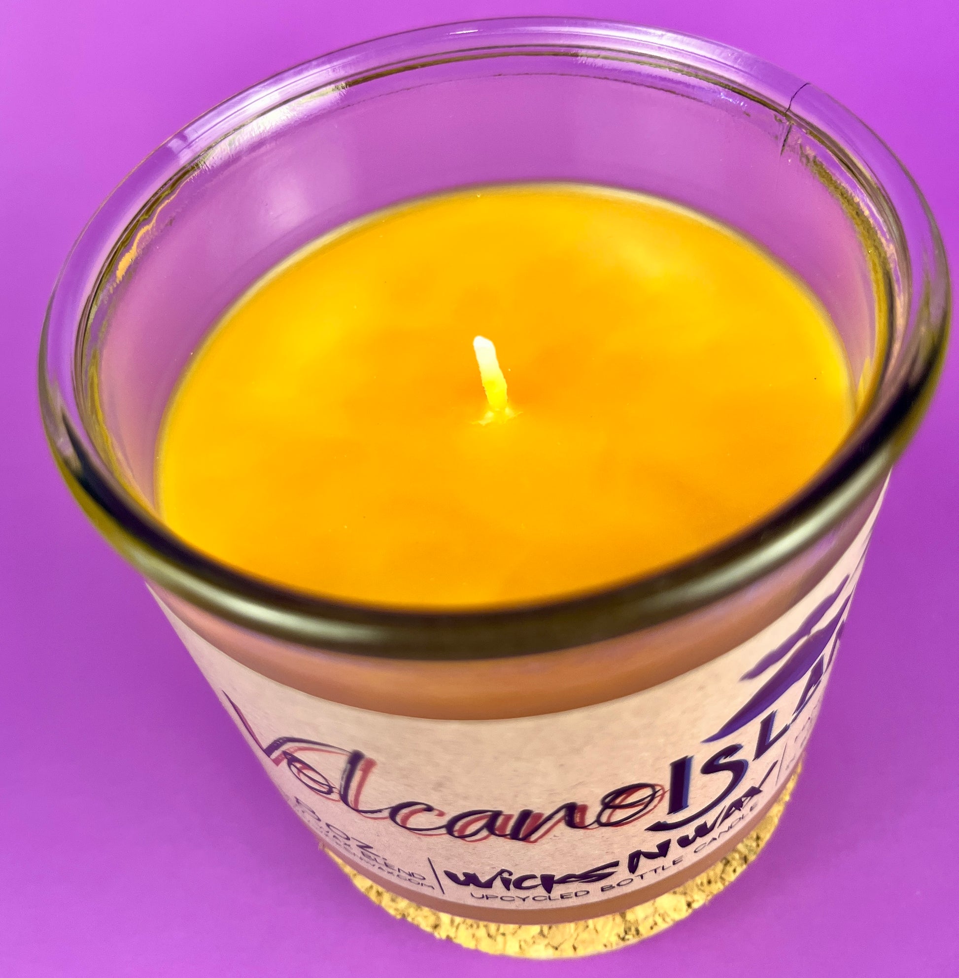 Yellow wax candle close-up with small flame wick inside Volcano Island glass jar