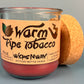 Glass bottle candle with red wax, leaf-and-smoke graphic label, cork lid behind