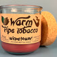 Glass bottle candle with red wax and leaf-and-smoke graphic label, cork lid behind