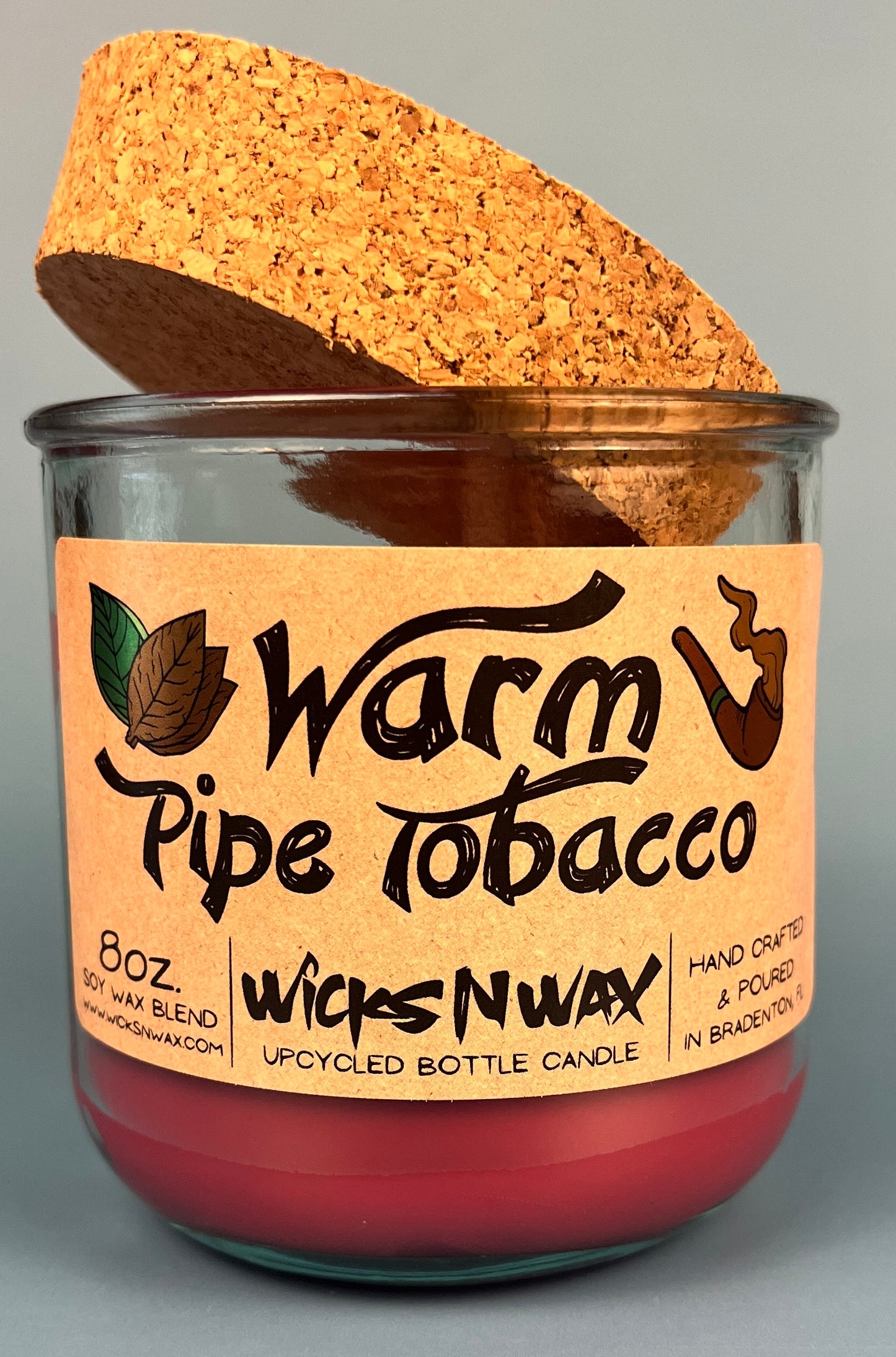 Glass bottle candle with red wax, leaf-and-smoke graphic label, with cork lid