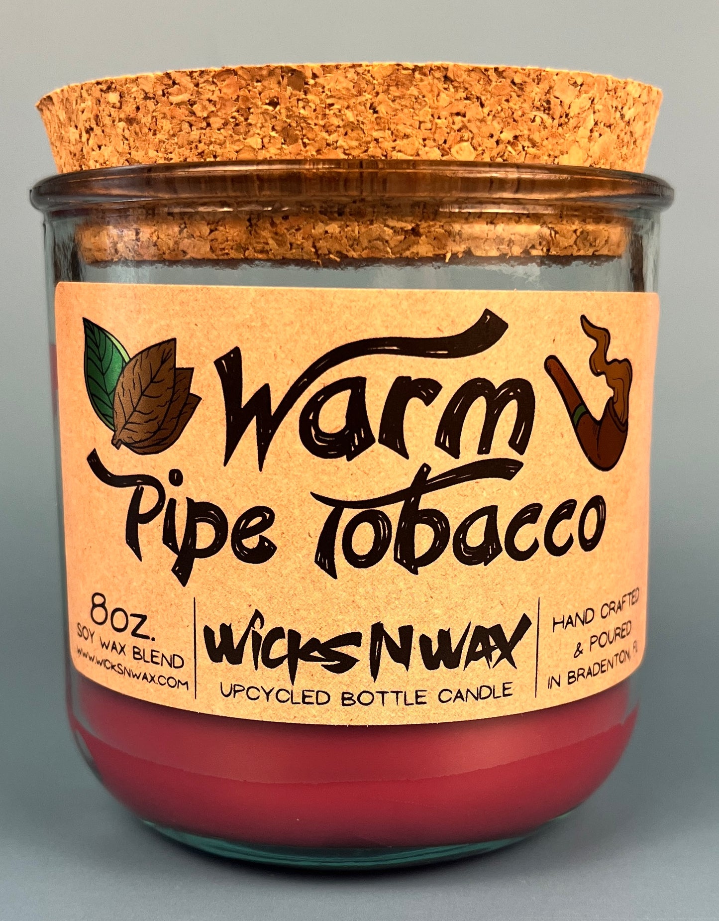Glass bottle candle with red wax, leaf-and-smoke graphic label, cork top exposed