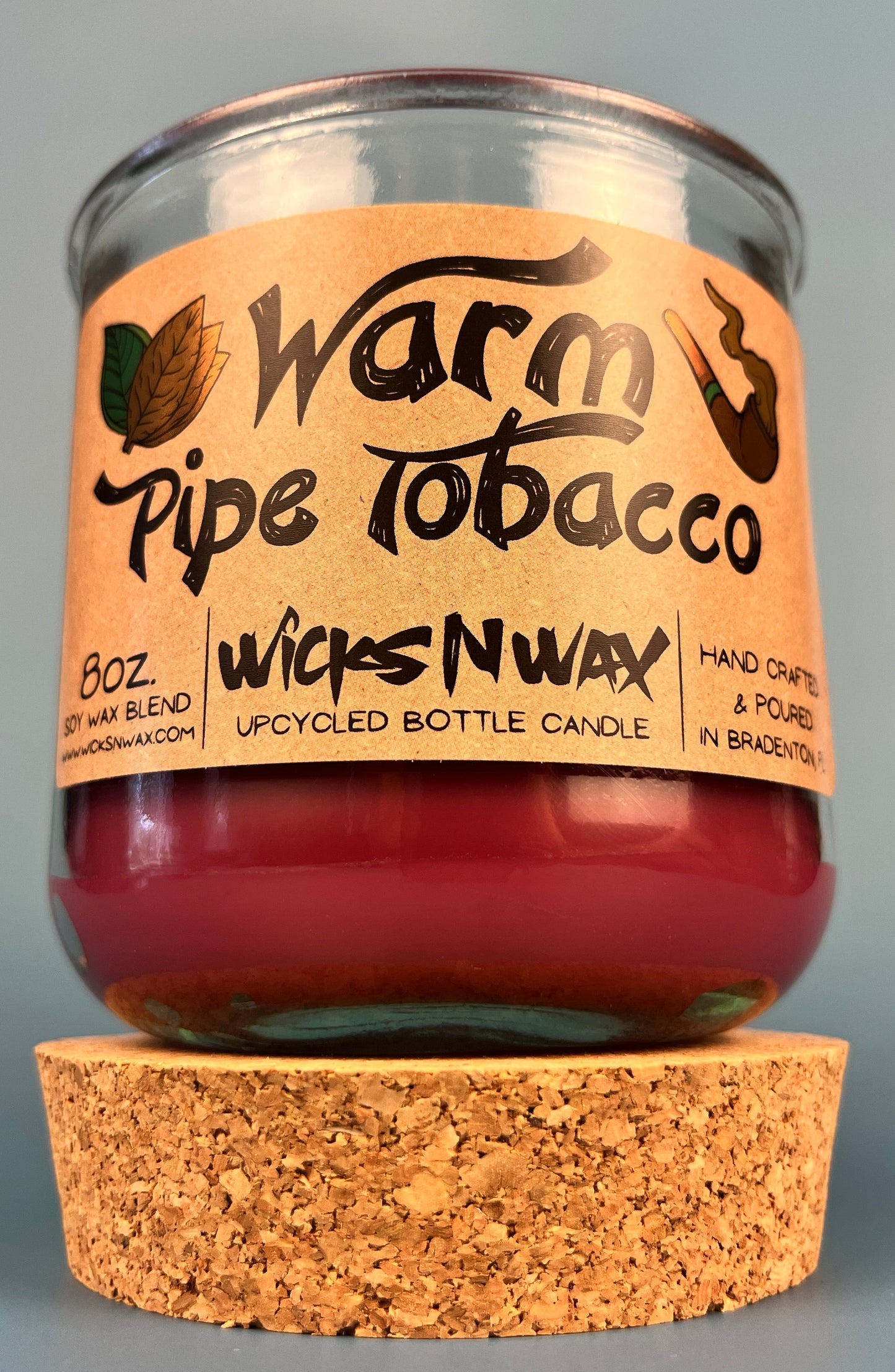 Glass bottle candle with red wax, leaf-and-smoke graphic label, and cork base