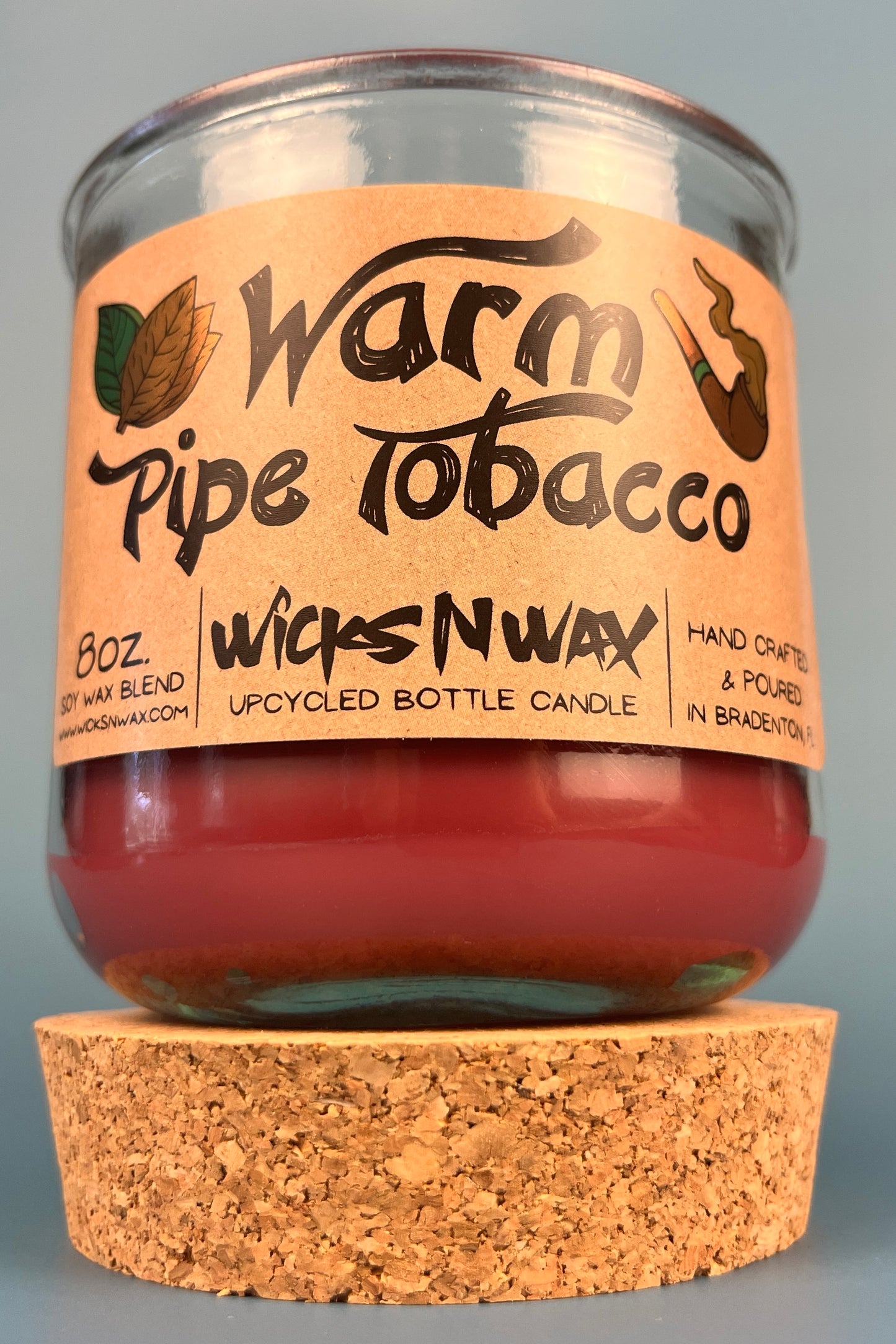 Glass jar bottle candle with red wax and leaf-and-smoke graphic label, on cork base