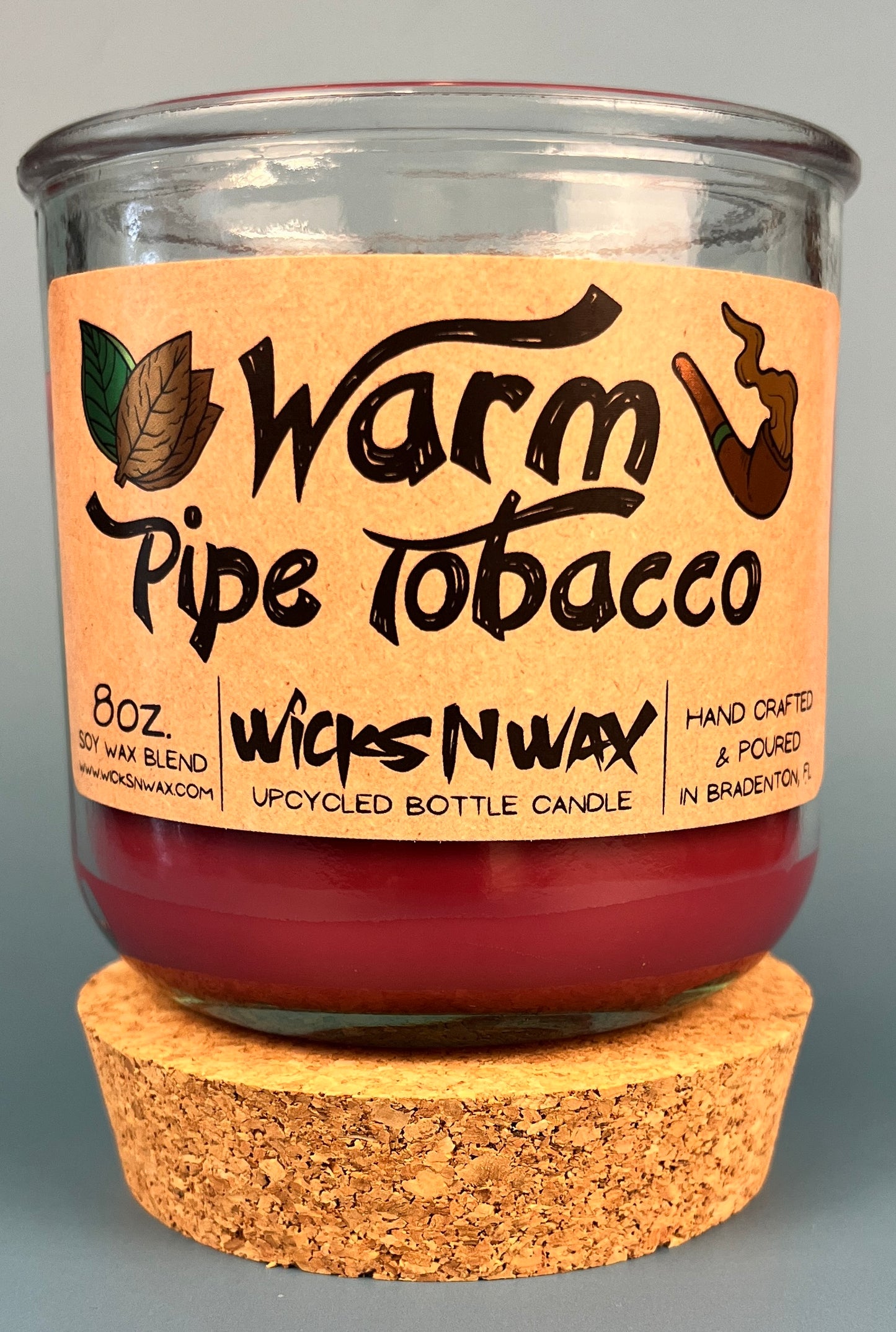 Glass bottle candle with red wax, leaf-and-smoke graphic label, on cork base