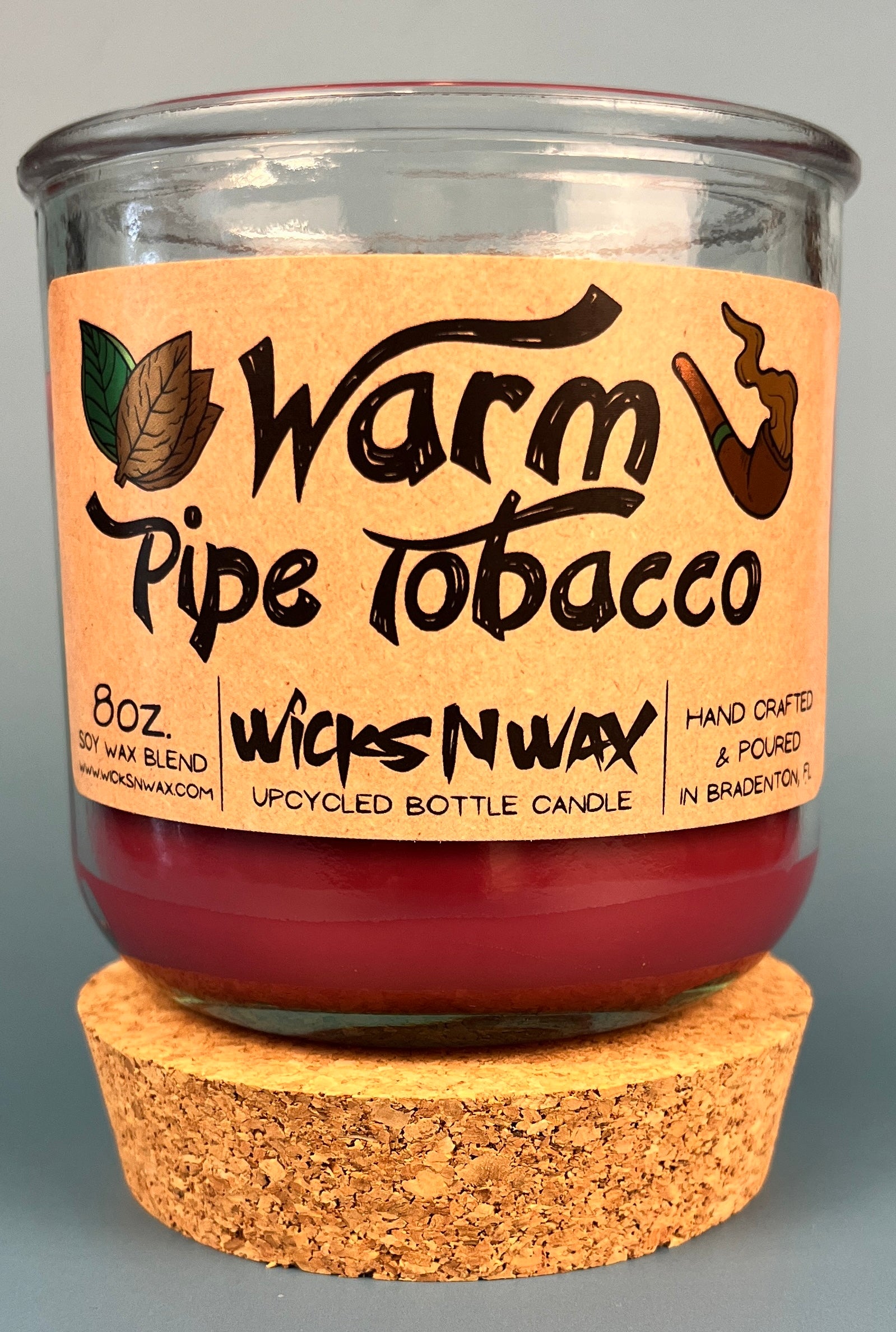 Glass bottle candle with red wax, leaf-and-smoke graphic label, on cork base