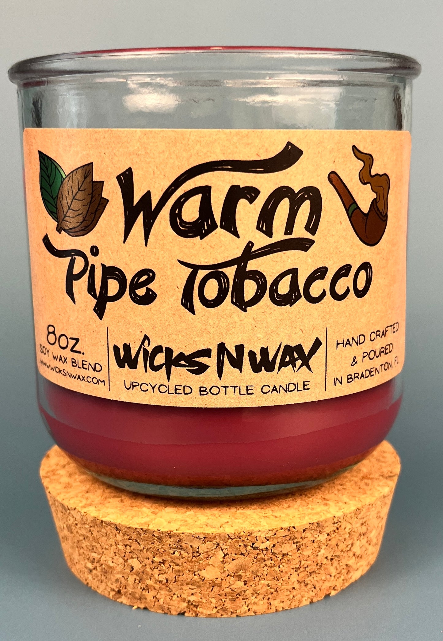 Glass bottle candle with red wax, leaf-and-smoke graphic label, on cork base