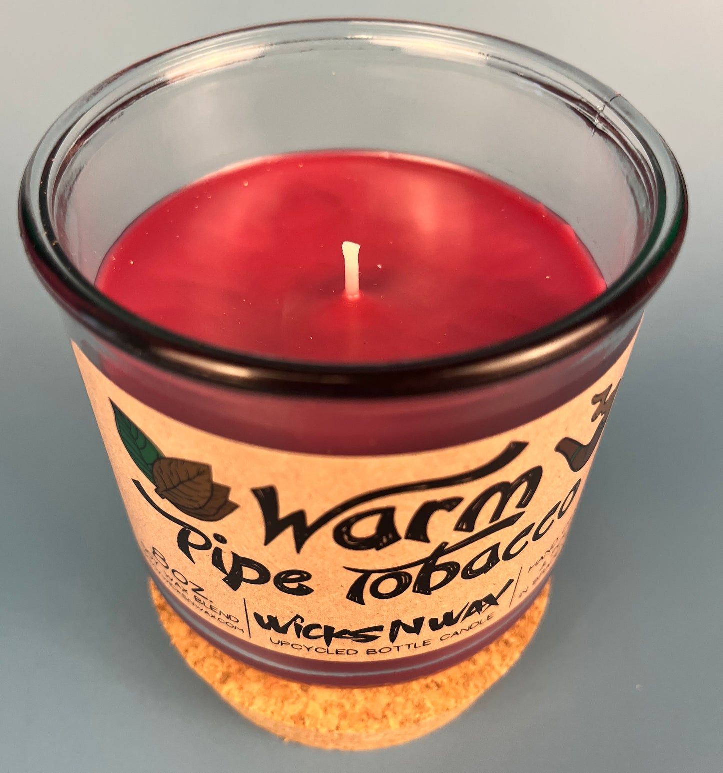 Glass jar candle top view with red wax and centered wick, leaf-and-smoke label